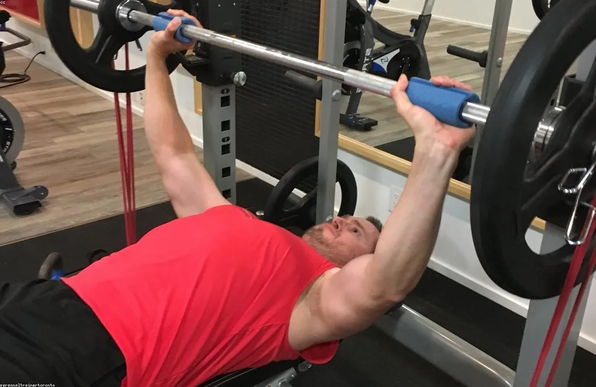 Member bench-pressing a barbell with a coach close by